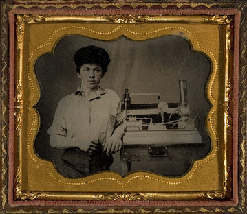 Unidentified young man, posed with model of steam driven engine on a table, ca. 1865
